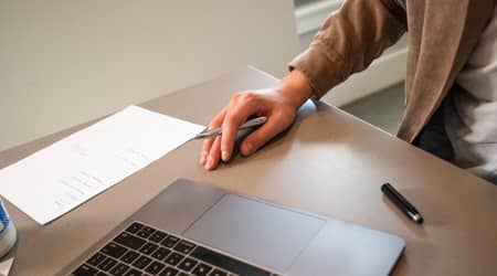 Osoba siedząca przy biurku, na którym stoi laptop