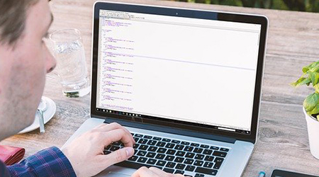 Zdjęcie przedstawiające mężczyznę siedzącego przed laptopem. Ujęcie wykonane zza głowy mężczyzny.