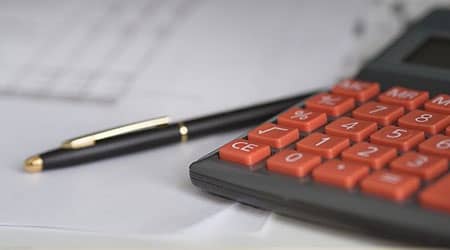 Zdjęcie przedstawiające kalkulator, długopis i kartki papieru.