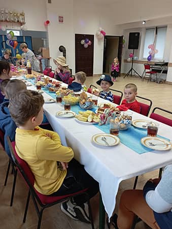 Zdjęcie przedstawiające dzieci siedzące przy stoliku z poczęstunkiem.