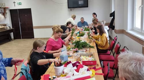 Zdjęcie grupy osób siedzących przy stołach, tworzących ręczne ozdoby.