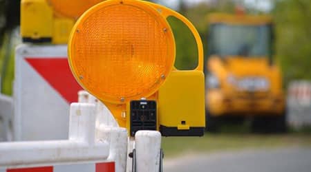 Zdjęcie bariery drogowej z oświetleniem. W tle ładowarka budowlana..