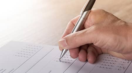 Zdjęcie dłoni trzymającej długopis i wypełniającej ankietę.