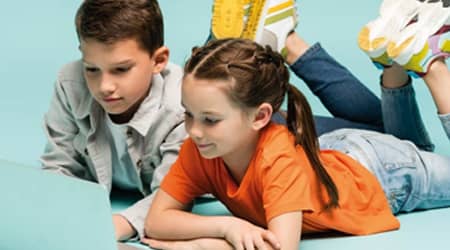 Zdjęcie dzieci leżących przed laptopem.