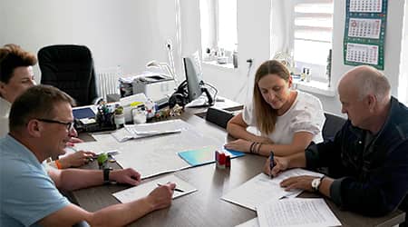 Źródło grafiki: UG Jonkowo Cztery osoby siedzące przy stole w gabinecie wójta podczas podpisywania dokumentów.