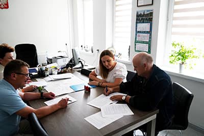 Cztery osoby siedzące przy stole w gabinecie wójta podczas podpisywania dokumentów.