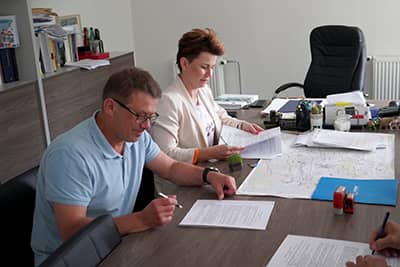 Kobieta i mężczyzna siedzą przy stole i podpisują dokumenty.