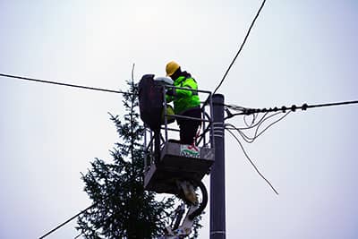 Pracownik montujący lampę oświetleniową, stojący w koszu wysięgnika.