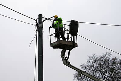Pracownik demontujący starą lampę oświetleniową, stojący w koszu wysięgnika.