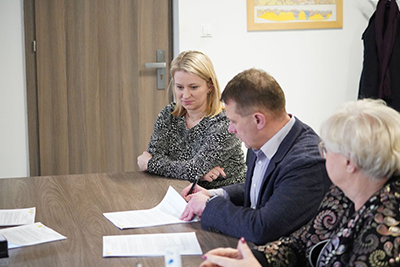 Trzy osoby siedzące przy stole. Mężczyzna i dwie kobiety. Mężczyzna podpisuje dokumenty.