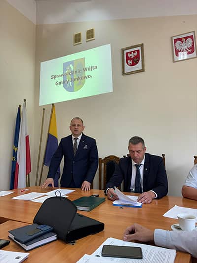 Zdjęcie dwóch osób. Jedna siedzi przy stole, druga przemawia na stojąco.