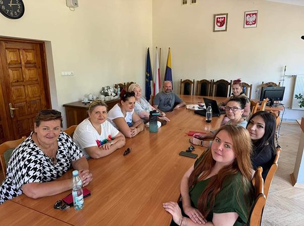 Grupa kobiet i jeden mężczyzna siedzący przy stole w sali sesyjnej