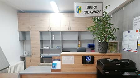 Zdjęcie. Widok biura podawczego. Lada, w tle szafki na dokumenty, z prawej strony kserokopiarka. Na boku lady - pętla indukcyjna dla osób niepełnosprawnych.