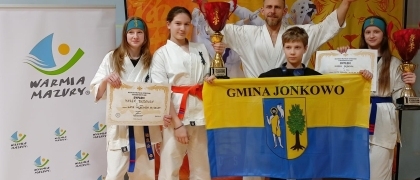zdjęcie przedstawia karateków z Akademii Sztuk Walki Jonkowo trzymających flagę Gminy Jonkowo